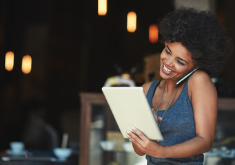 Success is the order of the day. Shot of a young woman using a digital tablet while talking on the phone at a cafe.