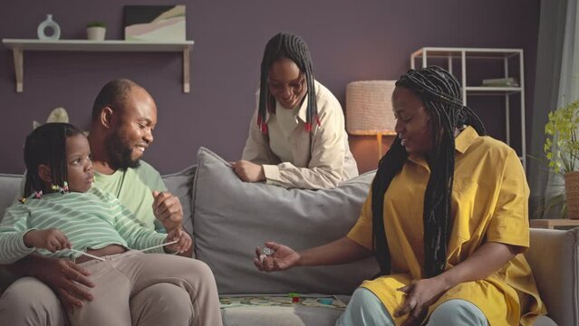 Happy Black family with two kids spending leisure time together at home playing boardgame on couch in living room