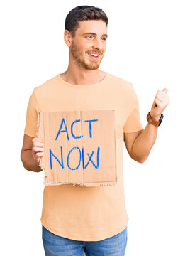 Handsome young man with bear holding act now banner pointing thumb up to the side smiling happy with open mouth