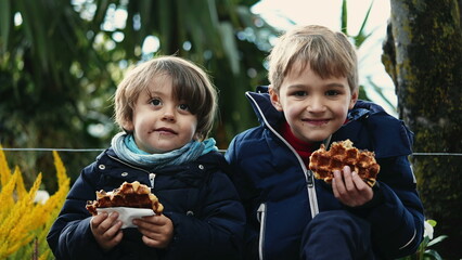 Two happy brothers eating belgium waffles outside
