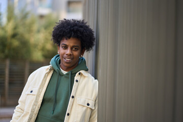 Smiling curly cool young African American guy model standing at big city street urban wall. Stylish...
