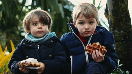Naklejka premium Two happy brothers eating belgium waffles outside