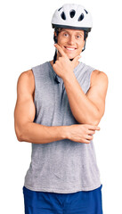 Young handsome man wearing bike helmet looking confident at the camera smiling with crossed arms and hand raised on chin. thinking positive.