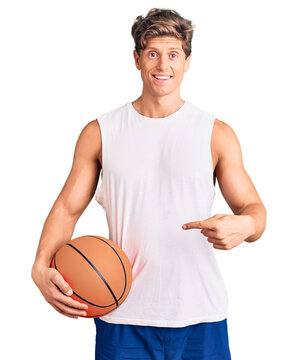 Young handsome man holding basketball ball smiling happy pointing with hand and finger