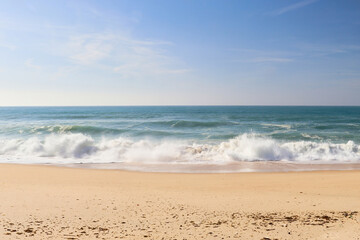Sandy beach with waves in the ocean near Lisbon, Portugal on a sunny winter day.