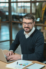 Obraz premium Smiling man in glasses typing on laptop in the office