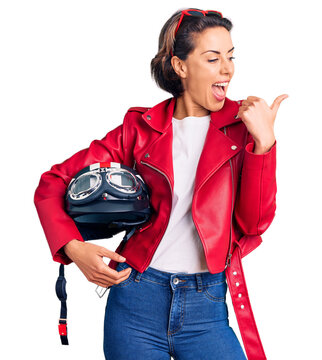 Young beautiful woman holding motorcycle helmet pointing thumb up to the side smiling happy with open mouth