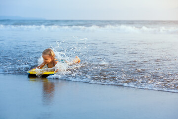 Little baby girl - young surfer with bodyboard has fun on sea beach. Family lifestyle, people outdoor water sport lessons and swimming activity on summer vacation with child in adventure surf camp.