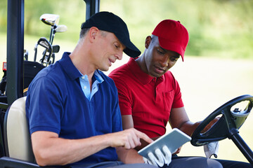 Getting the best golfing tips online. Shot of two men in a golf cart looking at a digital tablet.