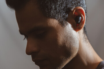 hombre joven latino de piel trigueña usando y mostrando audífonos bluetooth en fondo neutro y...