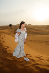 Fototapeta na wymiar A young beautiful woman posing in a dress - against the background of a desert landscape. Abu Dhabi, UAE.