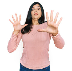 Young hispanic woman wearing casual clothes afraid and terrified with fear expression stop gesture with hands, shouting in shock. panic concept.
