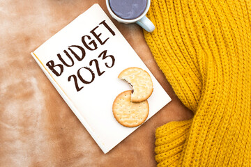 2023 budget text on notebook with cookies above bed, cup of coffee