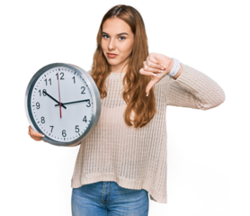 Young blonde woman holding big clock with angry face, negative sign showing dislike with thumbs down, rejection concept