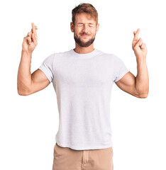 Young caucasian man wearing casual white tshirt gesturing finger crossed smiling with hope and eyes...