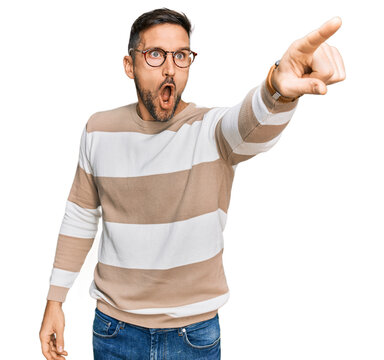 Handsome Man With Beard Wearing Casual Clothes And Glasses Pointing With Finger Surprised Ahead, Open Mouth Amazed Expression, Something On The Front