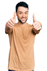 Hispanic man with beard wearing casual t shirt approving doing positive gesture with hand, thumbs up smiling and happy for success. winner gesture.