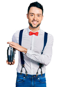 Hispanic man with beard preparing cocktail mixing drink with shaker smiling with a happy and cool smile on face. showing teeth.