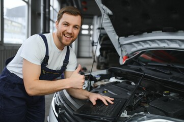 With laptop. Adult man in uniform works in the automobile salon.