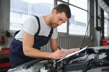 car mechanic writing while holding clipboard near cars