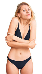 Young beautiful blonde woman wearing bikini shaking and freezing for winter cold with sad and shock expression on face