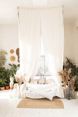 Bed with pillows, wooden furniture, plants in pots, an armchair and curtains on large windows in a...