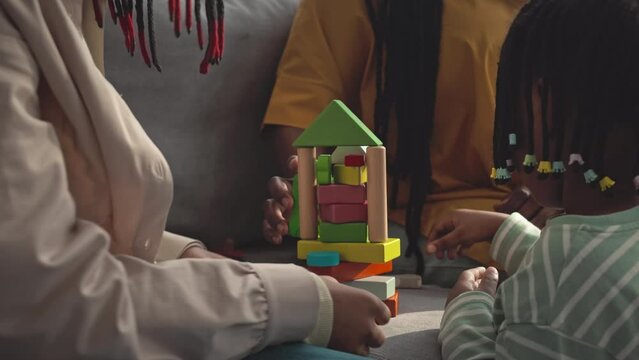 Cropped shot of unrecognizable Black woman with two little daughters playing with colorful construction and building blocks on couch at home