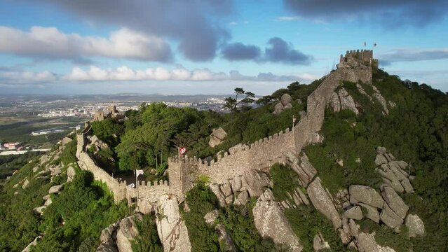 Aerial view of the town of Sintra in Portugal, historical Castelo Dos Mouros (moors castle) fortress, walls and Pena Palace in the summer, taken with a drone, on a beautiful green summit rocky hilltop