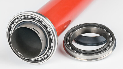 Steel single-row ball bearing in red metal print drum on white background. Closeup of rolling element on hollow pressure roller of dismantled fuser unit from inside of copier machine or laser printer.