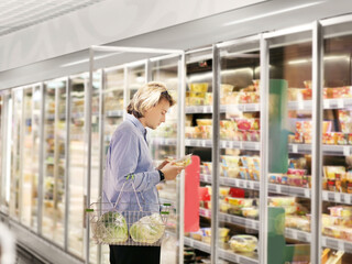  Man choosing frozen food from a supermarket freezer., reading product information