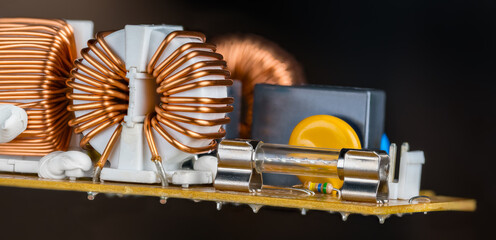 Glass electric fuse or toroid coils copper wire in hovering circuit board on black background. Close-up of inductors covered white plastic fixed by silicone paste on yellow PCB. Electronic components.