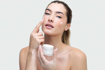 Beautiful young natural girl without makeup applies a cream to a face with fingers.