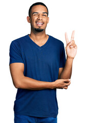 Young african american man wearing casual t shirt smiling with happy face winking at the camera doing victory sign. number two.