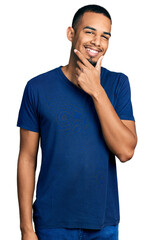 Fototapeta premium Young african american man wearing casual t shirt looking confident at the camera smiling with crossed arms and hand raised on chin. thinking positive.