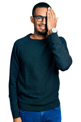 Fototapeta premium Young african american man wearing casual clothes and glasses covering one eye with hand, confident smile on face and surprise emotion.