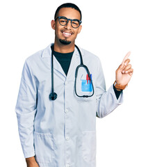 Young african american man wearing doctor uniform and stethoscope with a big smile on face, pointing with hand finger to the side looking at the camera.