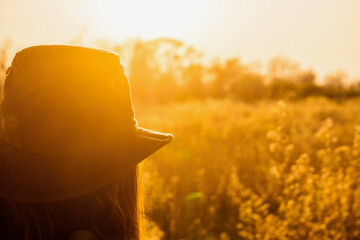 woman in hat looking at the sunrise over a field