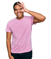 Young handsome hispanic man wearing casual pink t shirt smiling happy doing ok sign with hand on eye looking through fingers
