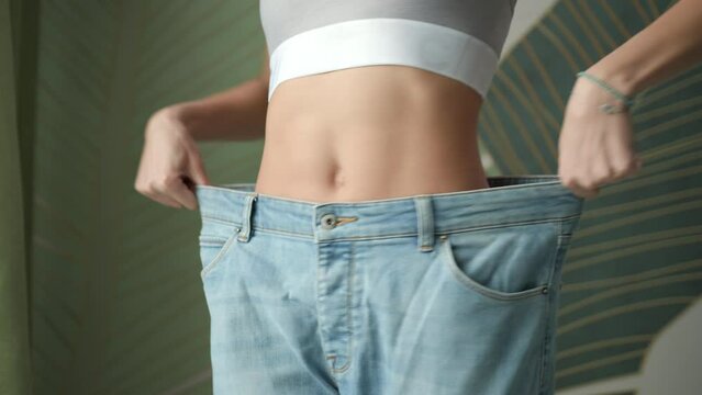 Woman Wearing Oversized Jeans. Slim female waist after weight loss. Loosing weight successfully.