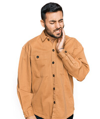 Young hispanic man wearing casual clothes touching mouth with hand with painful expression because of toothache or dental illness on teeth. dentist