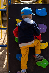 boy toddler climbing on the outdoor climbing wall in the playground