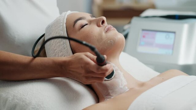 Video of  cosmetologist makes the procedure an ultrasonic cleaning of the facial skin of a beautiful young woman on the spa center.