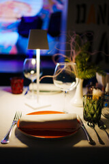a table with a white tablecloth, glasses, crockery and decor in dark restaurant