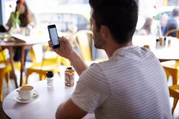 I got us a table. Shot of a man using his mobile phone while sitting at a restaurant table.