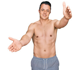 Fototapeta premium Handsome young man wearing swimwear shirtless looking at the camera smiling with open arms for hug. cheerful expression embracing happiness.