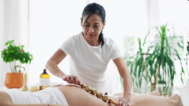 Video of therapist woman doing back massage with wooden balls to a pretty woman on the spa center