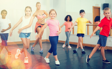 Fototapeta premium Group of tweens doing dance workout with female coach in classic choreography class..