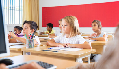 Group of preteen schoolchildren diligently working in class, making notes of teacher lecture