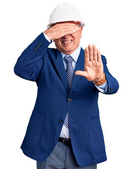 Senior handsome grey-haired man wearing suit and architect hardhat covering eyes with hands and doing stop gesture with sad and fear expression. embarrassed and negative concept.