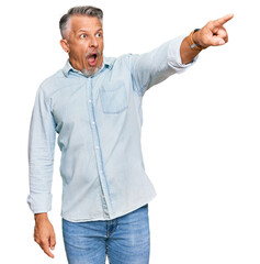 Middle age grey-haired man wearing casual clothes pointing with finger surprised ahead, open mouth amazed expression, something on the front